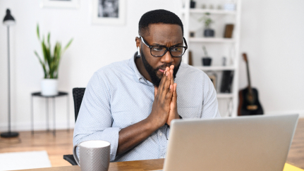 Man holding his hands together while looking at a laptop.