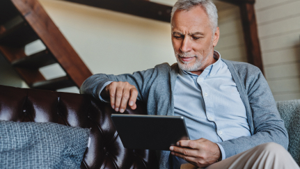 Man with a gray beard looking at a tablet.