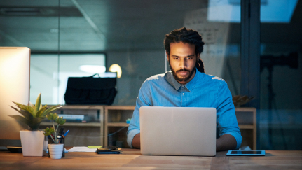 Man sitting behind a desk looking at a laptop.