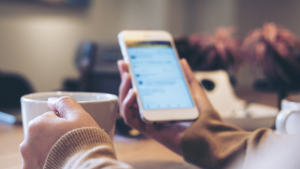 Hands holding a mug and a mobile phone.
