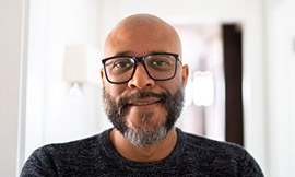 headshot of man with no hair, a beard, and glasses wearing a black shirt and smiling at the camera